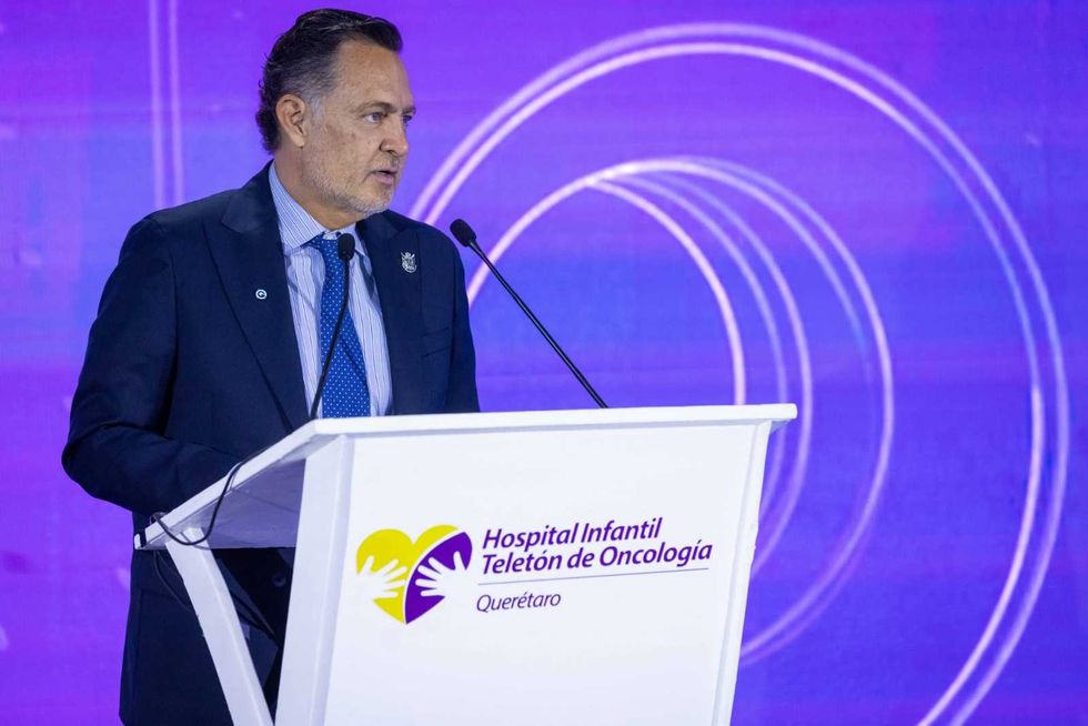 Hombre con saco azul marino habla en el podio del Hospital Infantil Telet\u00f3n de Oncolog\u00eda, frente a una pantalla con la ilustraci\u00f3n de un equipo m\u00e9dico, en la inauguraci\u00f3n de la radioterapia adaptativa.