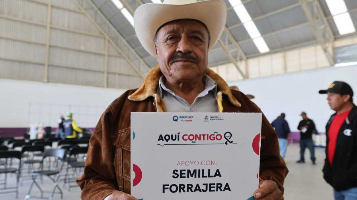 Hombre con sombrero blanco sostiene un letrero de apoyo con semilla forrajera en la entrega de apoyos en El Marqués