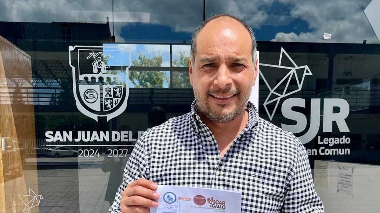 Hombre de camisa de cuadros sostiene la iniciativa sobre el descuento en traslado de dominio frente a la puerta de cristal de un edificio municipal de San Juan del Río.