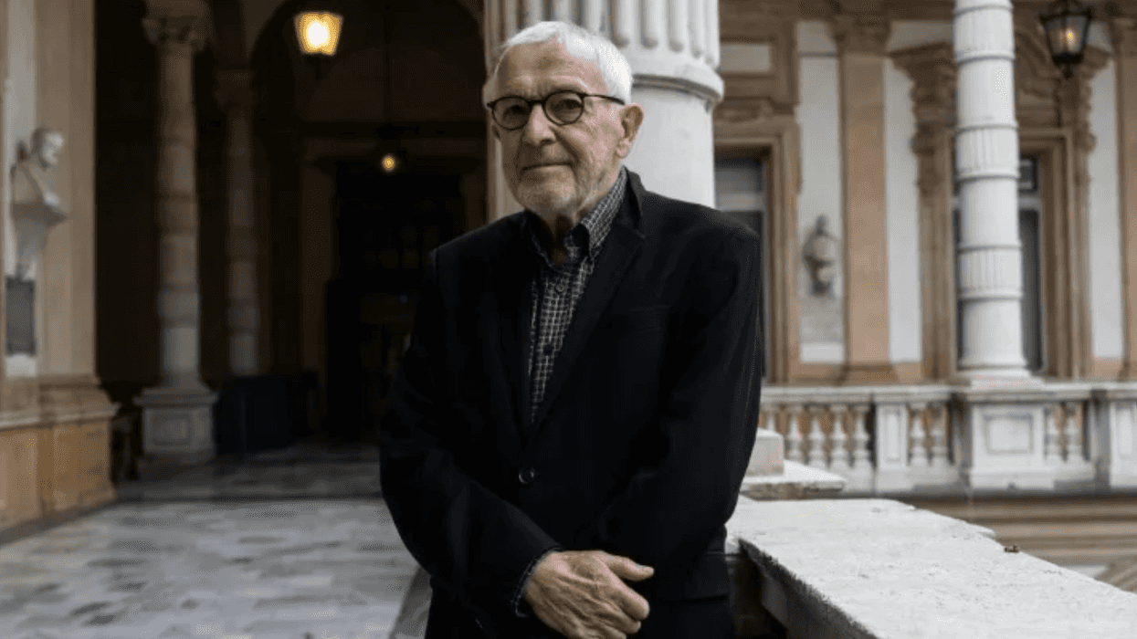 Hombre mayor de cabello blanco y lentes, con saco oscuro, en una galería con columnas; nota sobre neutrinos y IA