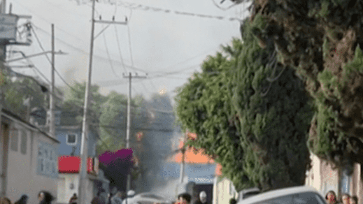 Humo y resplandor anaranjado tras los árboles de una calle de Coacalco durante la explosión en una gasera