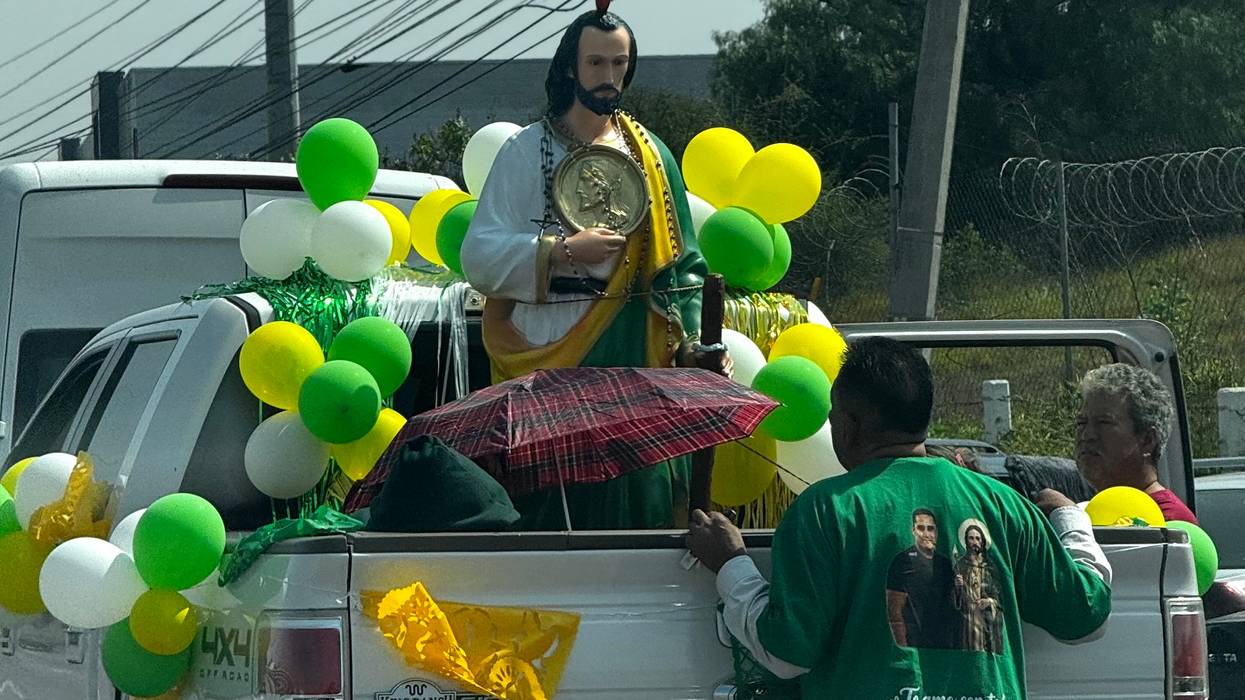 Imagen de San Judas Tadeo con medalla de Cristo al pecho, adornada con globos verdes, amarillos y blancos en la caja de una camioneta, durante la festividad en La Noria, El Marqués.
