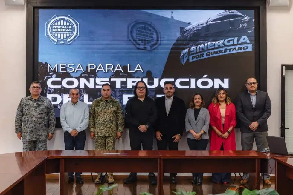 Integrantes de la Mesa para la Construcci\u00f3n de la Paz posan frente a la pantalla con los emblemas de la Fiscal\u00eda y de Sinergia por Quer\u00e9taro