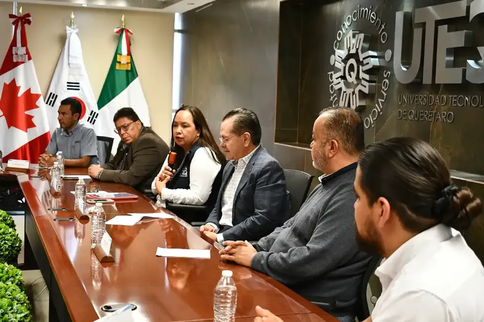 Integrantes del pres\u00eddium durante la presentaci\u00f3n del convenio entre la UTEQ y TREMEC, con banderas de Canad\u00e1, Corea del Sur y M\u00e9xico al fondo.