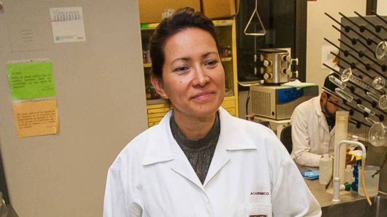 Investigadora con bata blanca en un laboratorio donde trabaja otra persona