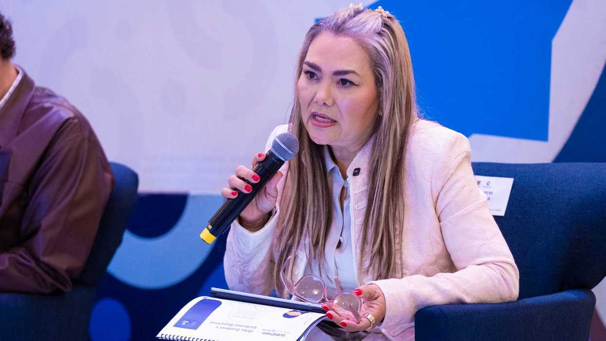 Irene Quintanar Mejía, coordinadora general de la USEBEQ, habla con un micrófono durante un evento, sentada y con unos lentes en la mano.