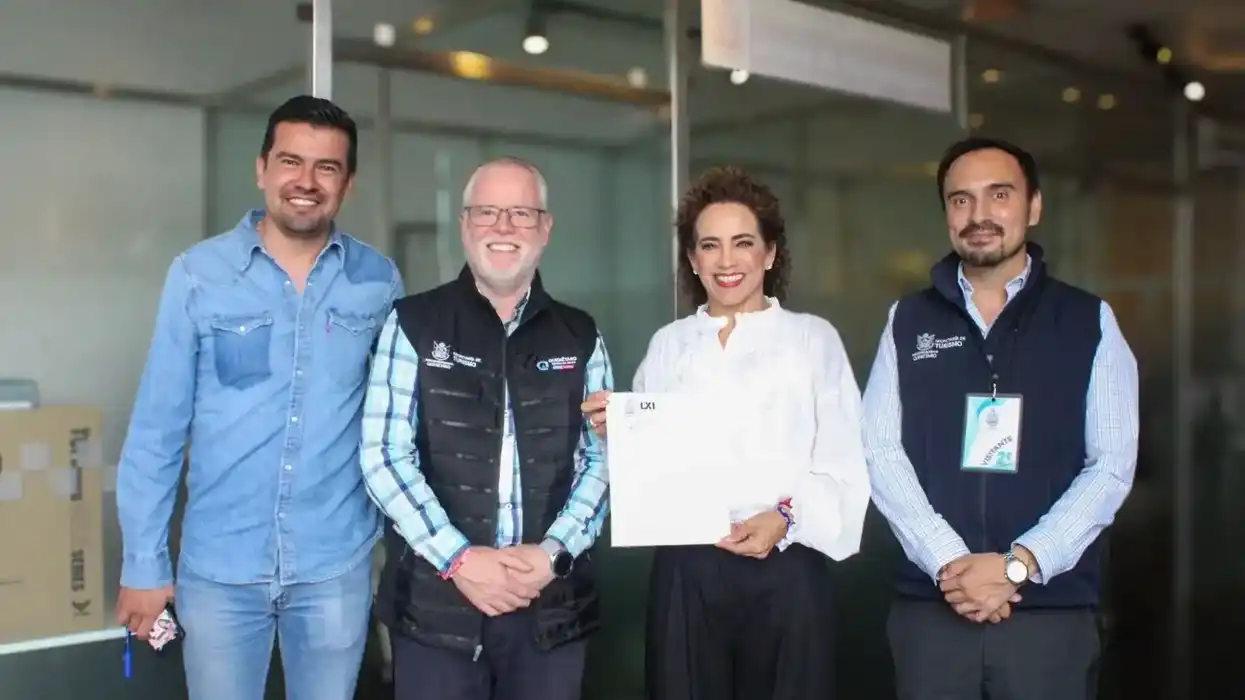 La diputada Adriana Meza sostiene un documento junto a tres hombres, dos con chaleco de la Secretaría de Turismo de Querétaro, en un pasillo institucional