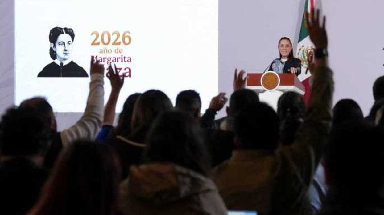 La presidenta Claudia Sheinbaum en el podio de la conferencia matutina, con reporteros de frente levantando la mano y una pantalla con la leyenda “2026 año de Margarita Maza”.