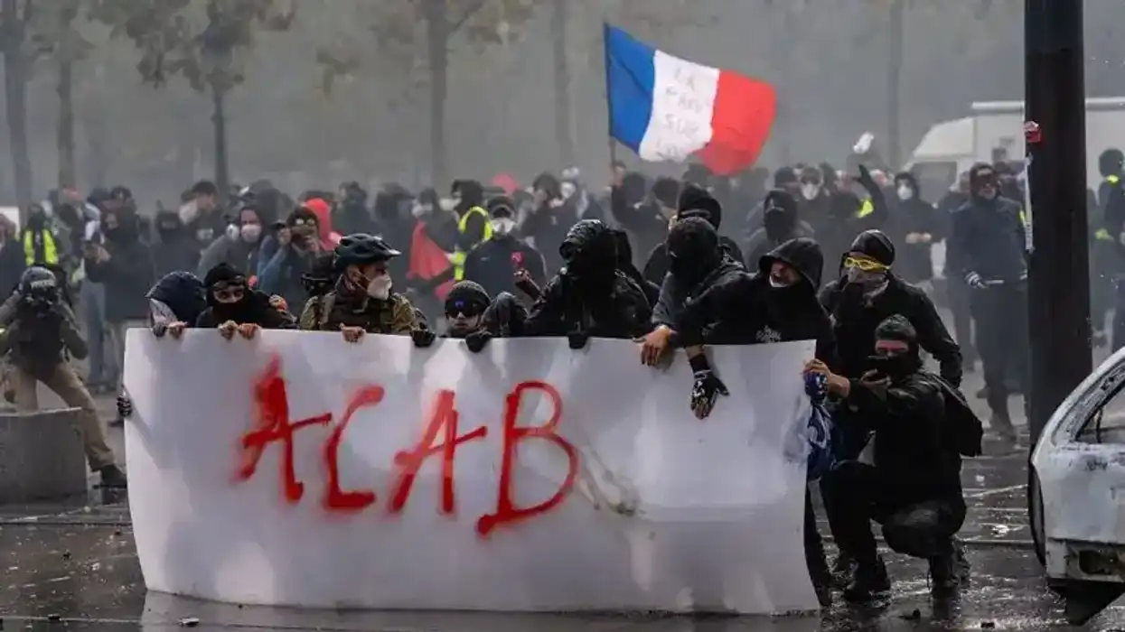 Manifestantes con rostro cubierto tras una pancarta con la leyenda ACAB y una bandera francesa entre humo