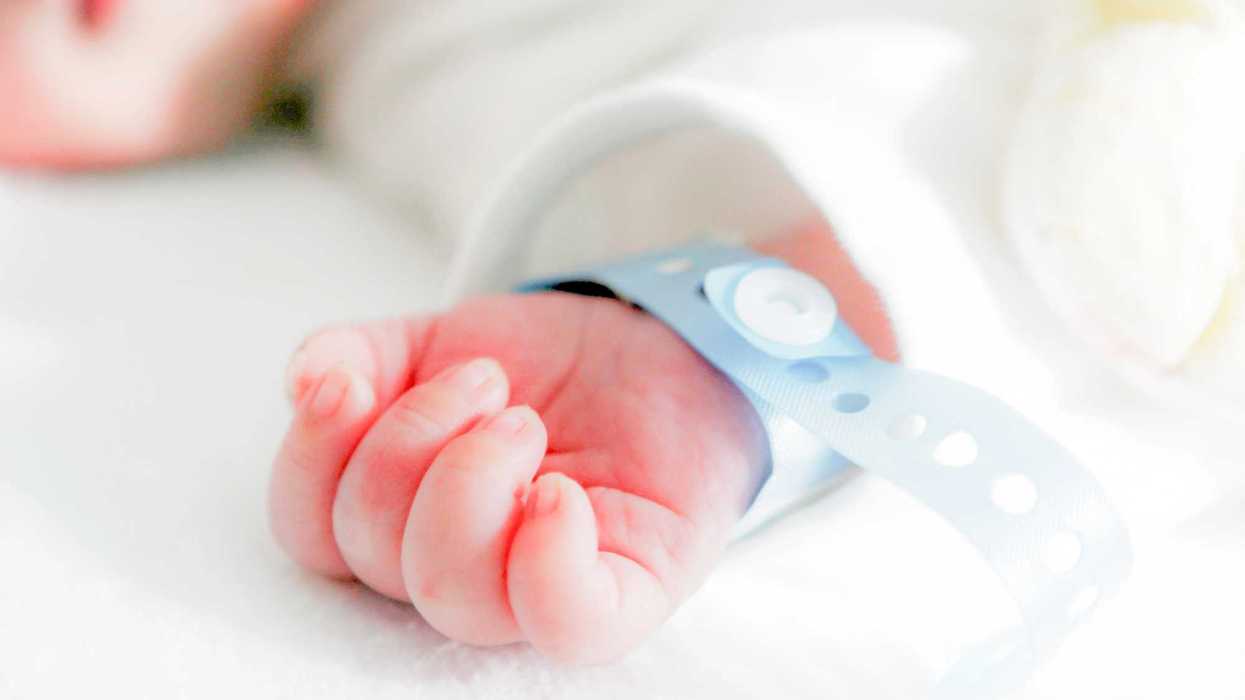 Mano de un recién nacido con brazalete azul de identificación sobre ropa blanca; IMSS revisa 77 unidades neonatales