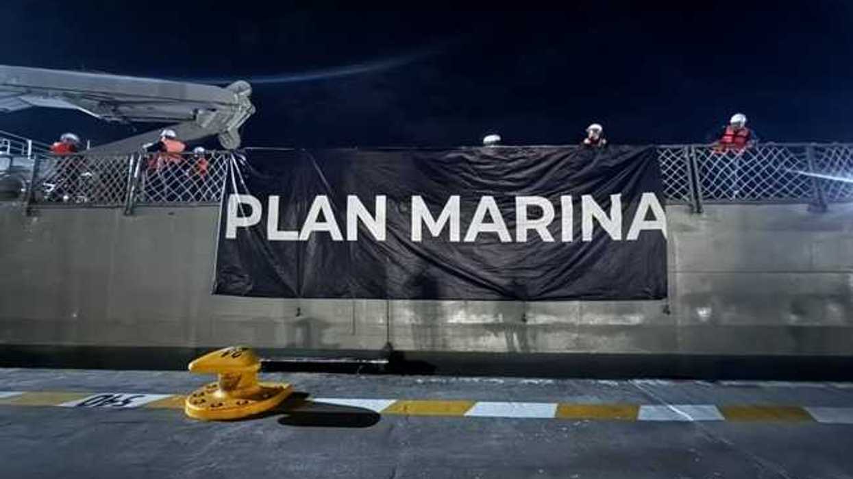Manta con la leyenda Plan Marina colgada en el costado de una embarcación, con personal naval a bordo durante la noche.