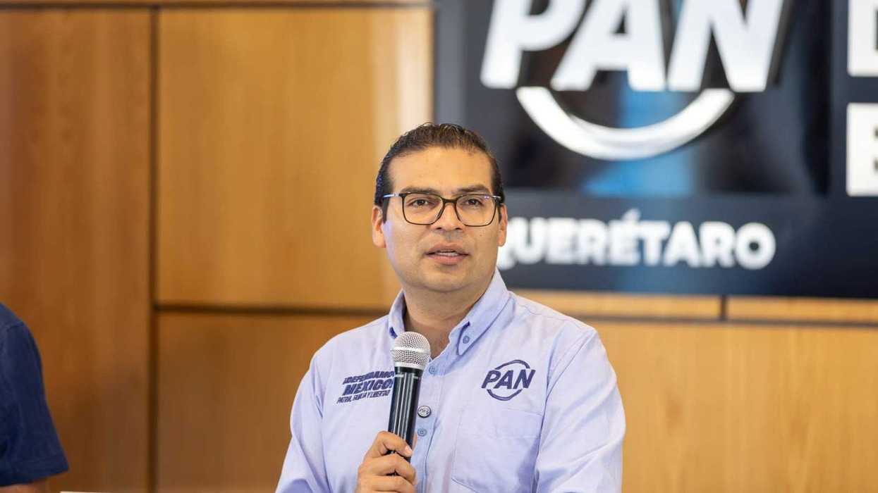 Martín Arango García, dirigente estatal del PAN en Querétaro, habla con un micrófono frente a un fondo con el logotipo del PAN Querétaro.
