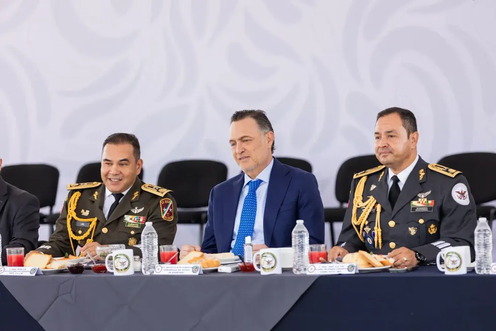 Mauricio Kuri Gonz\u00e1lez conversa en la mesa de honor flanqueado por dos mandos castrenses durante el acto conmemorativo