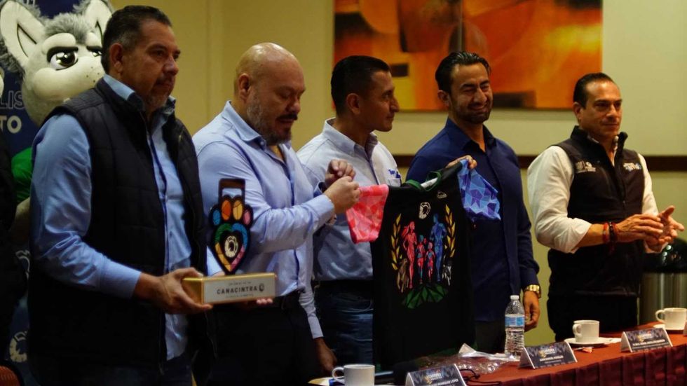Mesa de la conferencia de prensa de la carrera Canacintra en San Juan del R\u00edo, con una mascota y carteles