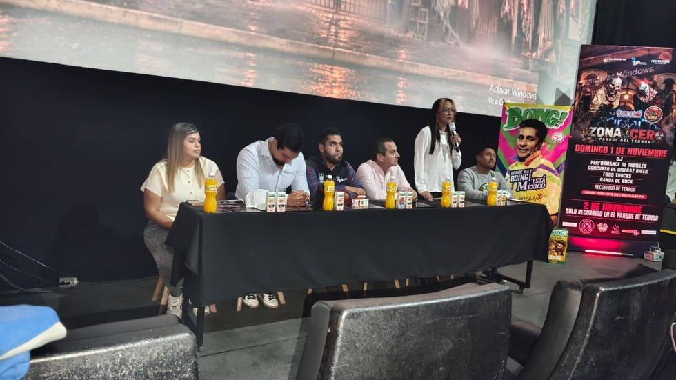 Mesa de presentaci\u00f3n de Zona Cero: Parque del Terror con una mujer hablando al micr\u00f3fono y seis personas sentadas