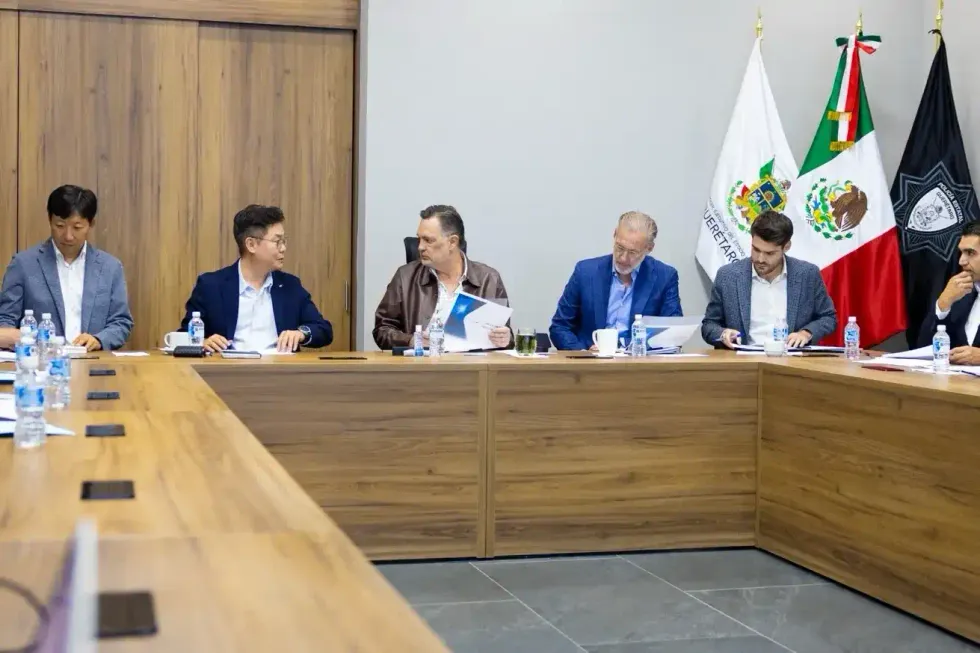 Mesa de trabajo con seis personas sentadas; banderas de Quer\u00e9taro, M\u00e9xico y otra instituci\u00f3n al fondo