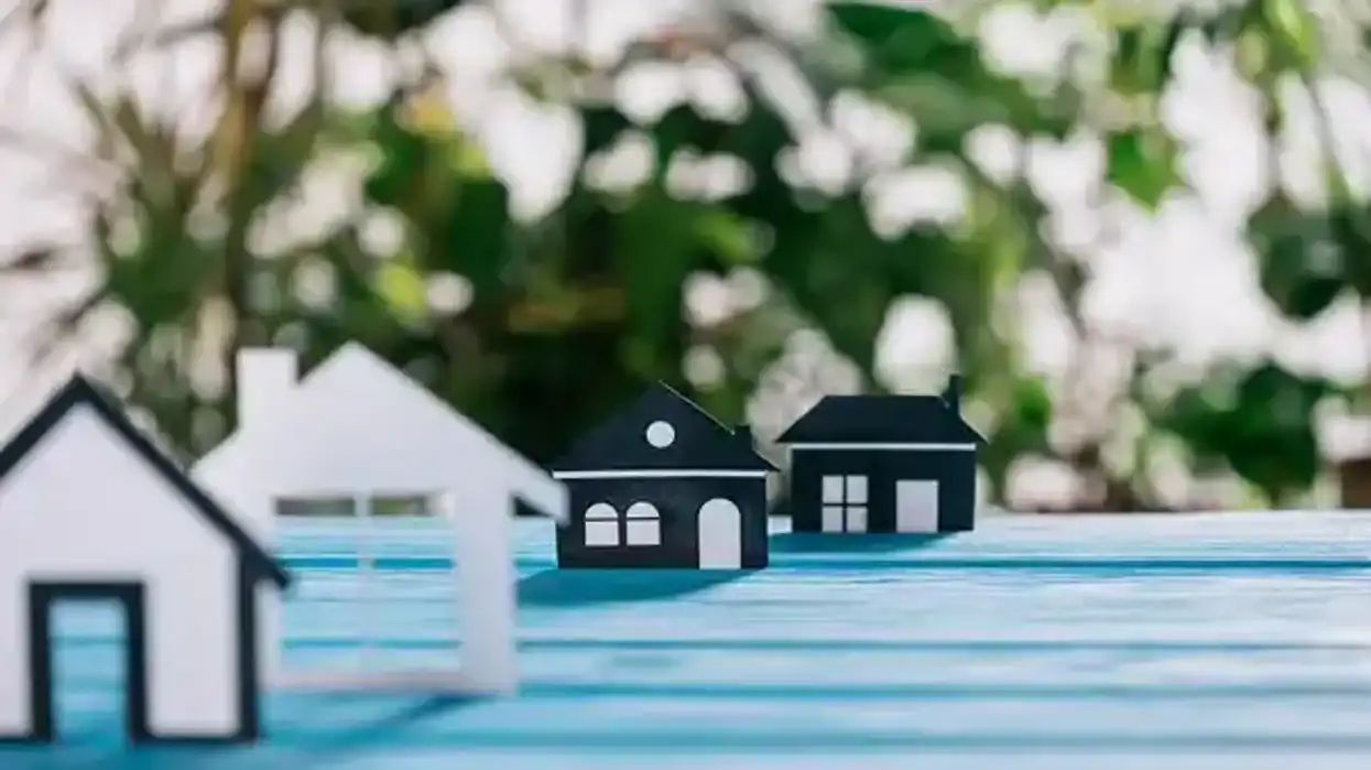 Miniaturas de casas de papel blancas y negras sobre superficie azul, ilustración editorial sobre regularización predial en San Juan del Río 2026.