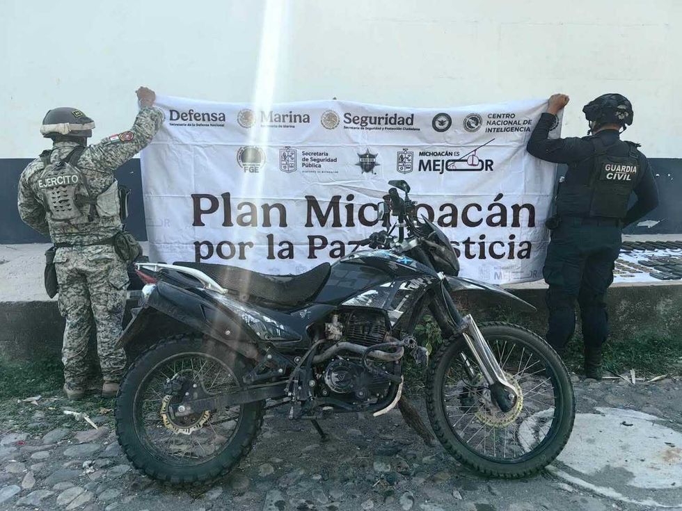 Motocicleta color negro estacionada frente a dos elementos de seguridad que sostienen una lona institucional