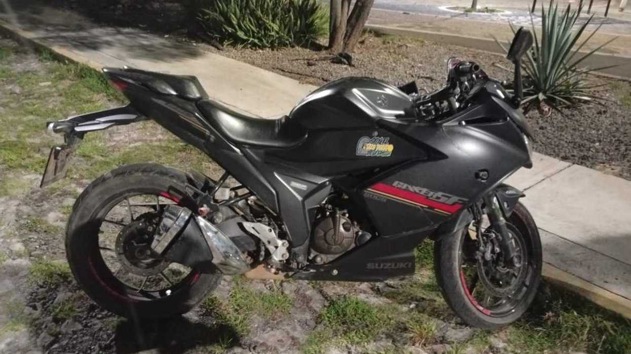 Motocicleta Suzuki negra sobre el pasto junto a una banqueta, con un área de juegos al fondo