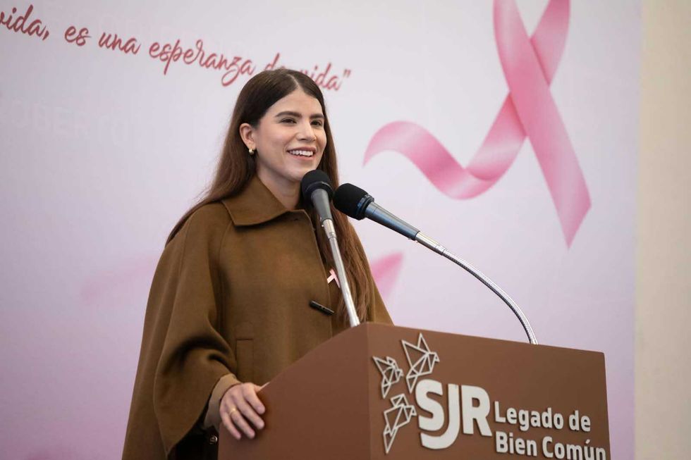 Mujer con abrigo caf\u00e9 habla desde el podio durante el XXIII Desayuno Anual de Grupo Reto en San Juan del R\u00edo