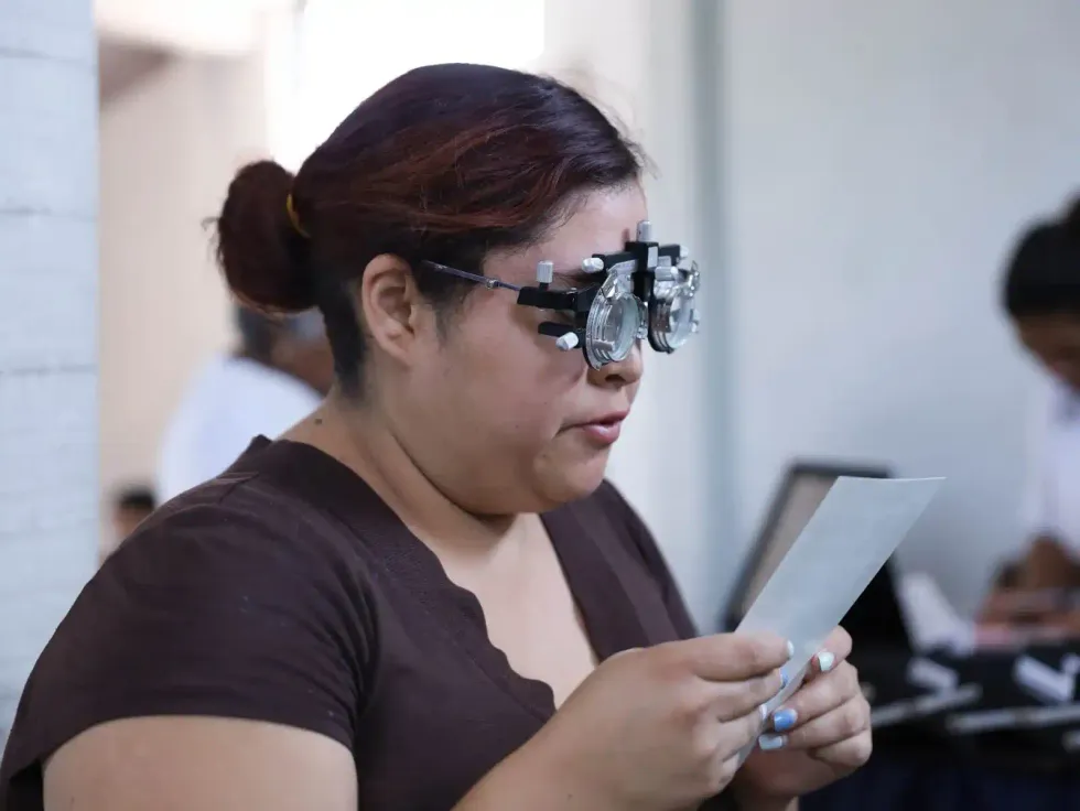 Mujer con armaz\u00f3n de optometr\u00eda lee una l\u00e1mina durante su examen de la vista en la campa\u00f1a de salud visual en El Mirador