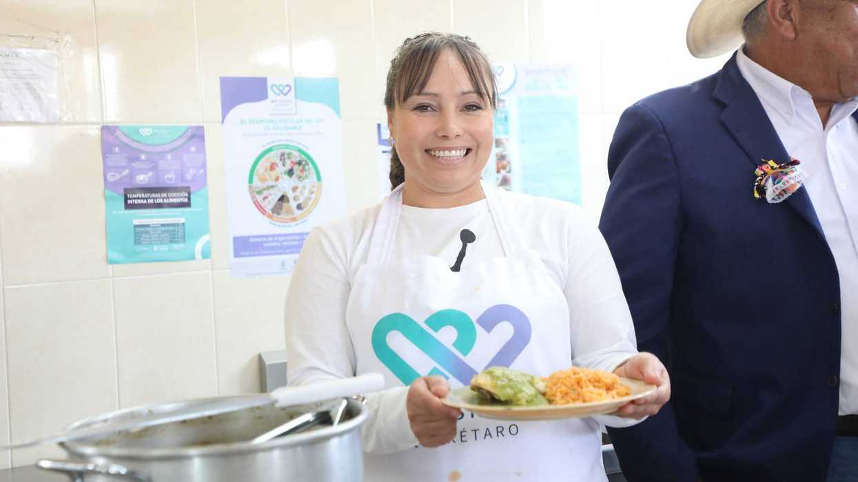 Mujer con delantal del DIF sostiene un plato con comida en el Aula Cocina de la Telesecundaria Leona Vicario, Amealco