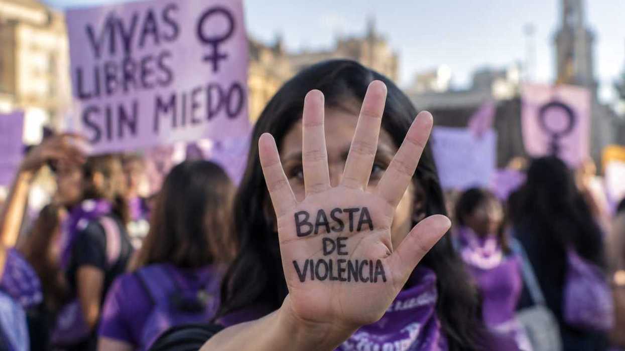 Mujer con la leyenda «Basta de violencia» escrita en la palma de la mano durante una marcha, con pancartas moradas al fondo