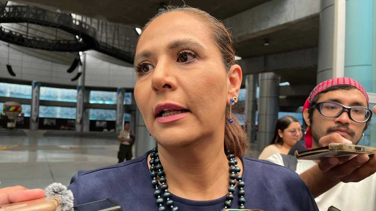 Mujer de blusa azul marino responde a reporteros que le acercan celulares, en entrevista sobre arcos detectores en escuelas