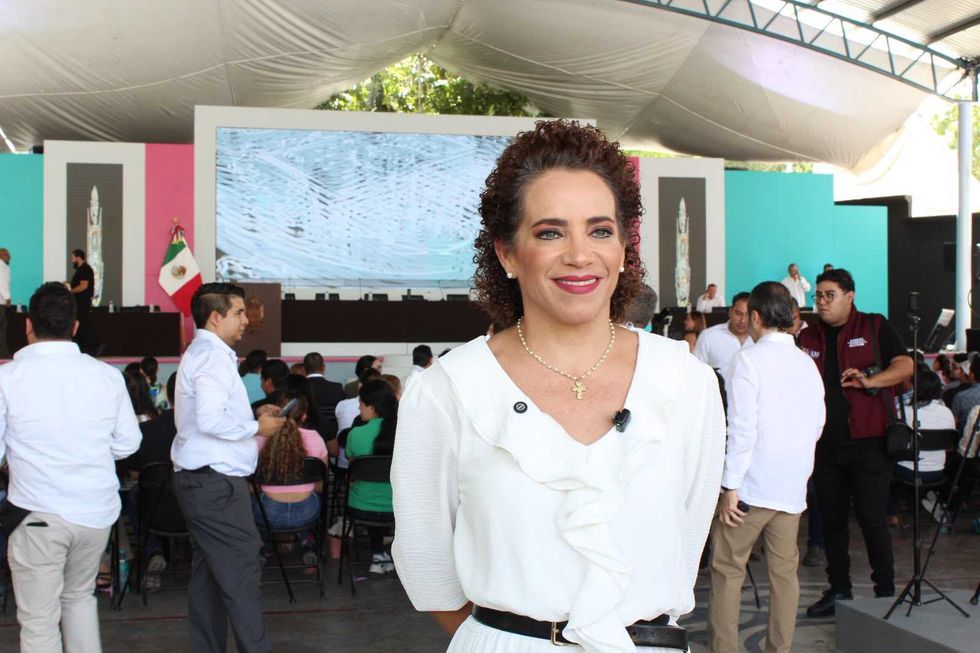 Mujer de blusa blanca sonr\u00ede frente al escenario del evento donde la Legislatura de Quer\u00e9taro aprob\u00f3 la reforma de turismo comunitario.