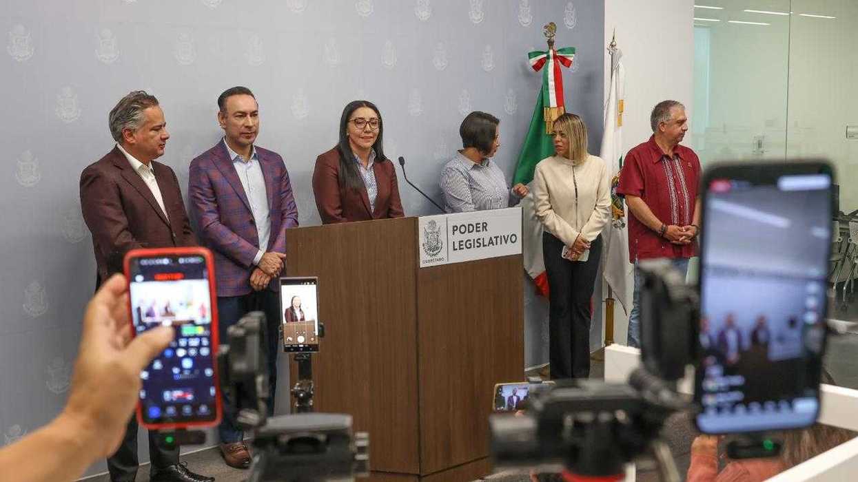 Mujer de blusa blanca sonríe frente al escenario del evento donde la Legislatura de Querétaro aprobó la reforma de turismo comunitario.
