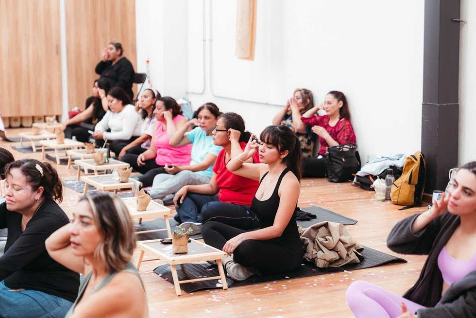 Mujeres sentadas en tapetes realizan un ejercicio con las manos en el rostro en el Centro de Empoderamiento, Quer\u00e9taro