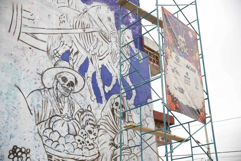 Muralista sobre un andamio pinta con rodillo el fondo del Mural de las \u00c1nimas de D\u00eda de Muertos en San Juan del R\u00edo