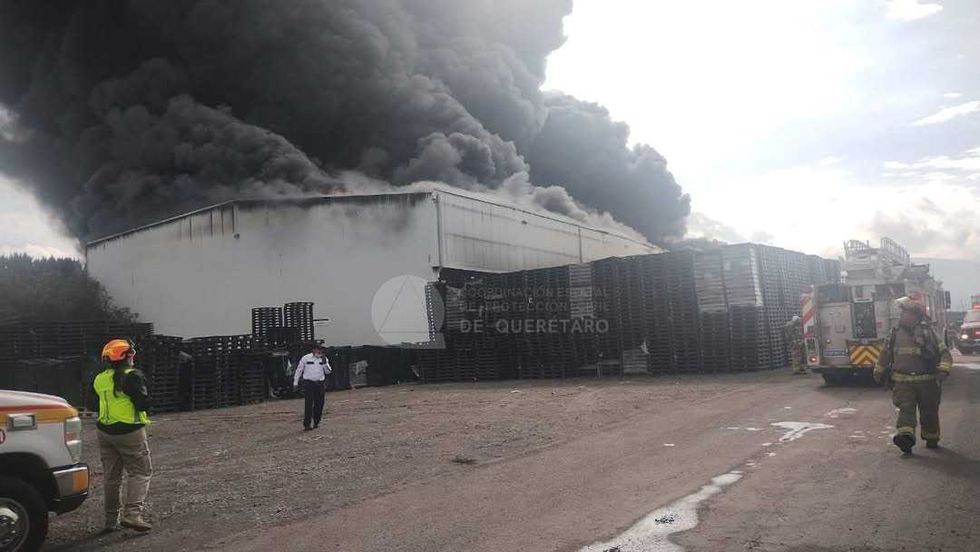 Nave industrial cubierta por una extensa columna de humo negro mientras unidades de emergencia permanecen en el exterior.