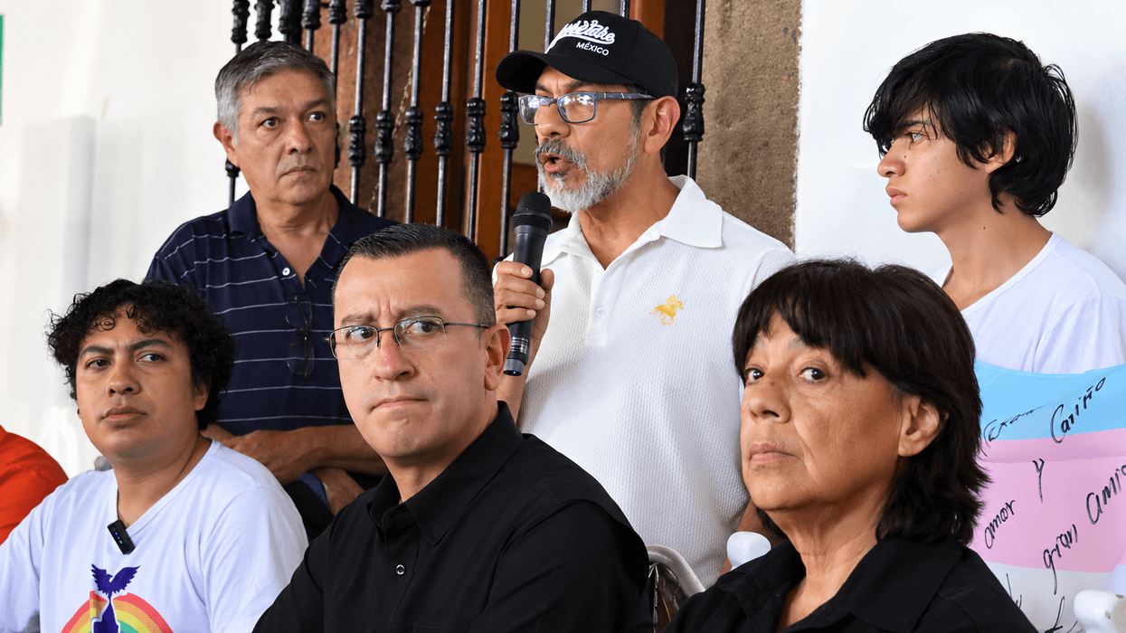 ntegrantes de colectivos LGBT+ en rueda de prensa sobre la Ley de Identidad de Género en San Juan del Río; un hombre con gorra habla al micrófono junto a una bandera trans con mensajes escritos.