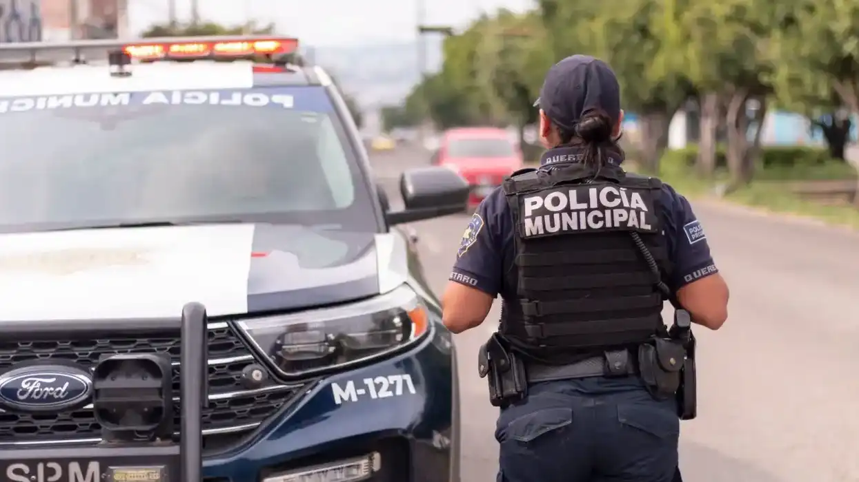 Oficial de la Policía Municipal de Querétaro camina junto a una patrulla en una vialidad