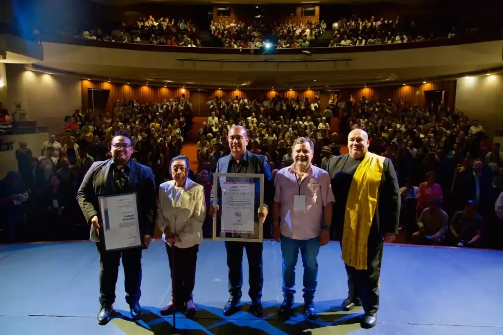 Organizadores y personas reconocidas posan sobre el escenario frente al p\u00fablico del teatro.