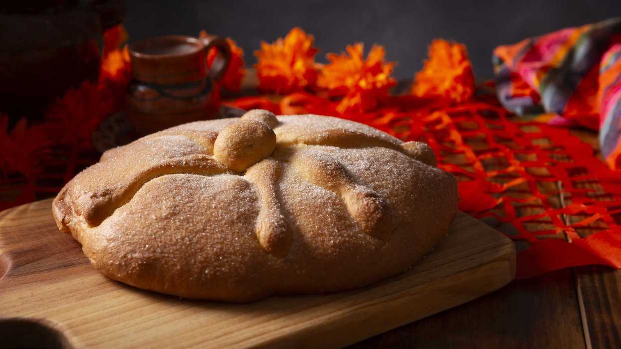 Pan de muerto con azúcar sobre tabla de madera junto a cempasúchil y papel picado rojo; concurso en San Juan del Río