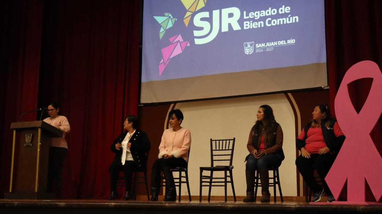 Panel de mujeres en el escenario junto a un moño rosa gigante durante la conferencia sobre cáncer de mama en San Juan del Río.
