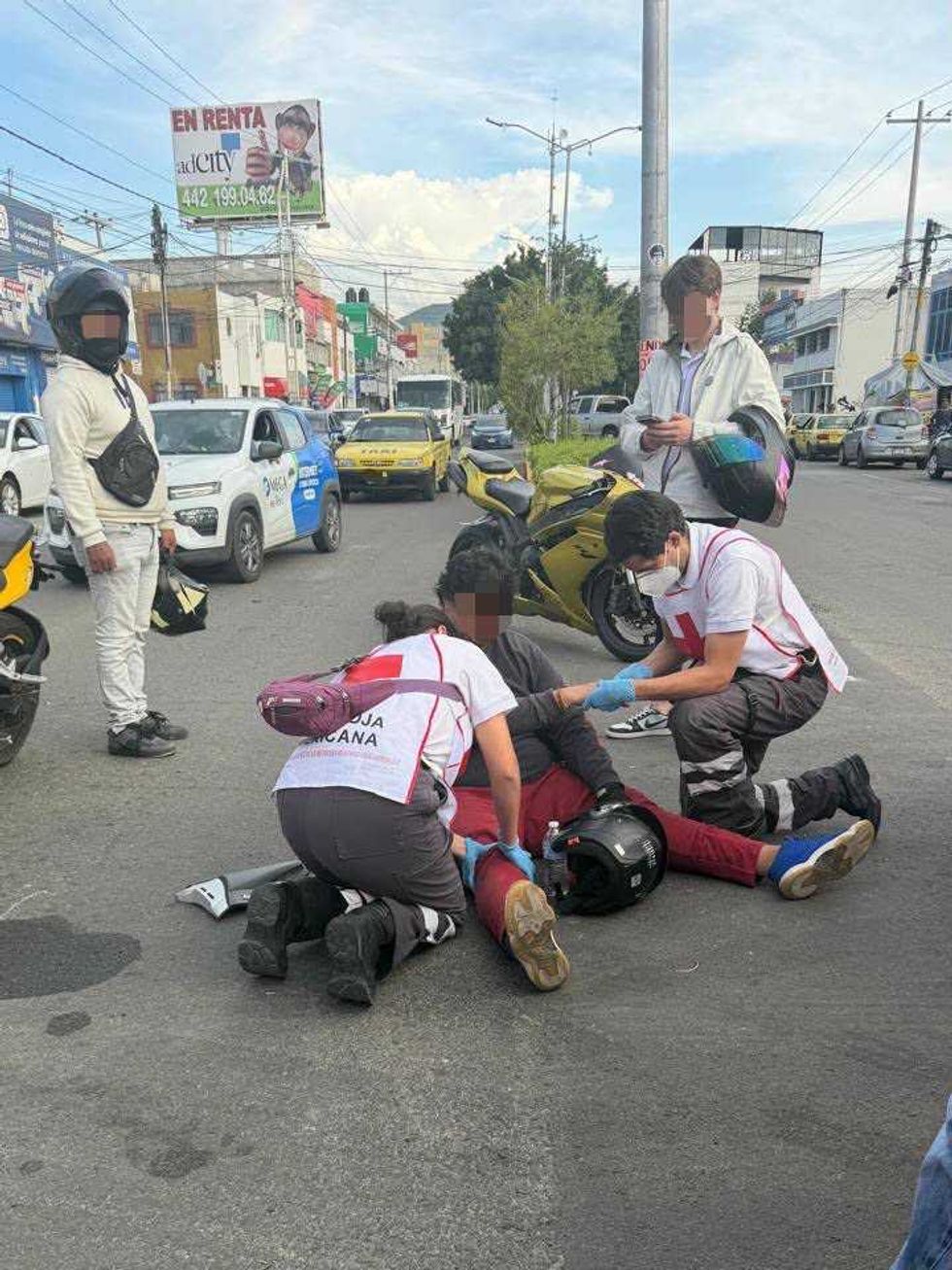 Param\u00e9dicos de la Cruz Roja Mexicana atienden en el piso a un motociclista con la pierna lesionada, junto a su motocicleta, en una vialidad de Quer\u00e9taro