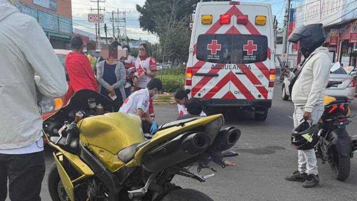 Paramédicos de la Cruz Roja Mexicana atienden en el piso a un motociclista con la pierna lesionada, junto a su motocicleta, en una vialidad de Querétaro