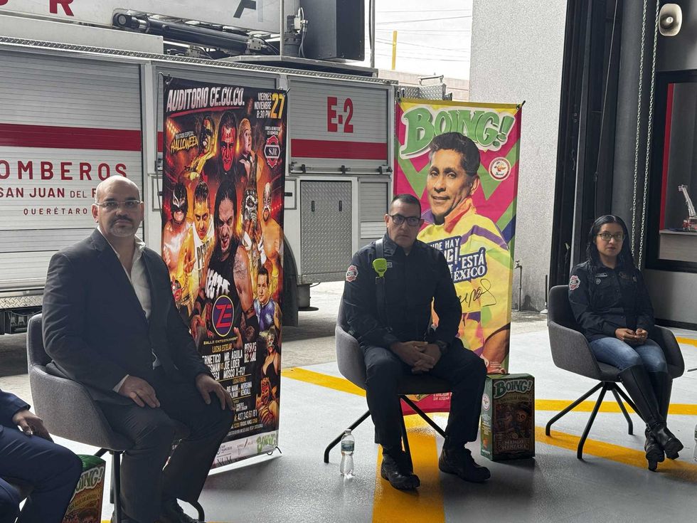 Participantes en la presentaci\u00f3n de la funci\u00f3n de lucha libre de Zalle Entertainment sentados junto al cartel del evento, en las instalaciones de Bomberos de San Juan del R\u00edo.