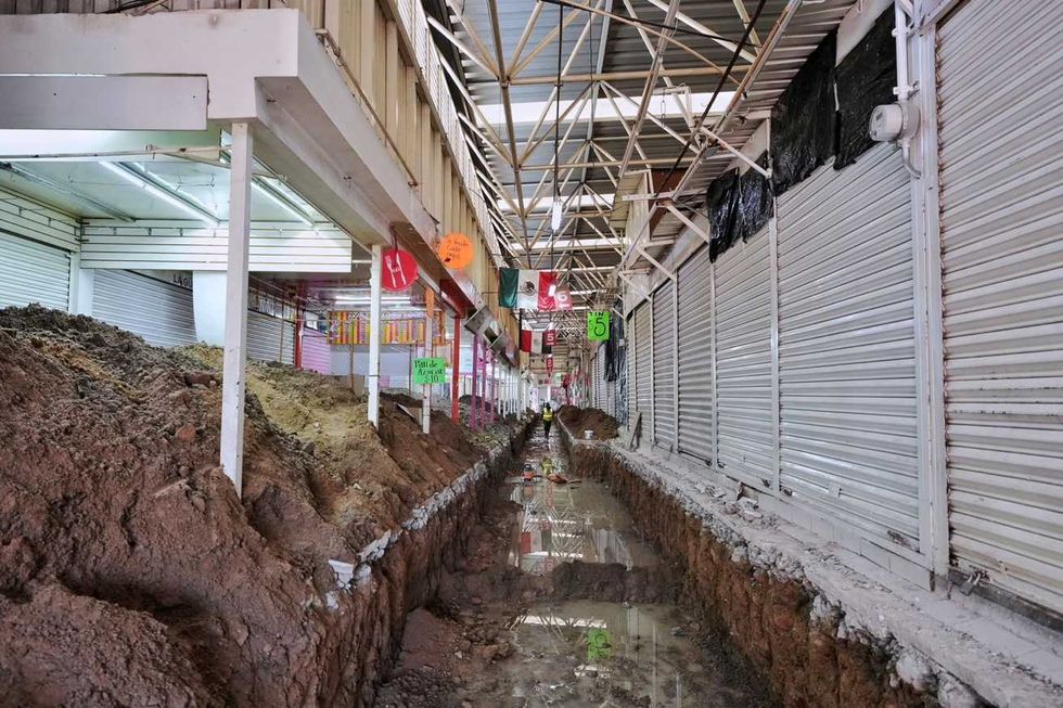 Pasillo del mercado Escobedo con una zanja de excavaci\u00f3n entre locales con cortinas met\u00e1licas cerradas