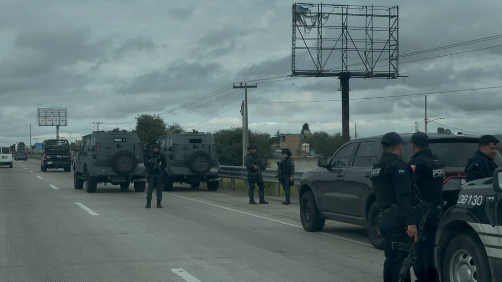 Patrulla de la Polic\u00eda Estatal con torretas encendidas y agentes armados frente a dos veh\u00edculos blindados detenidos en el acotamiento de la autopista M\u00e9xico-Quer\u00e9taro.