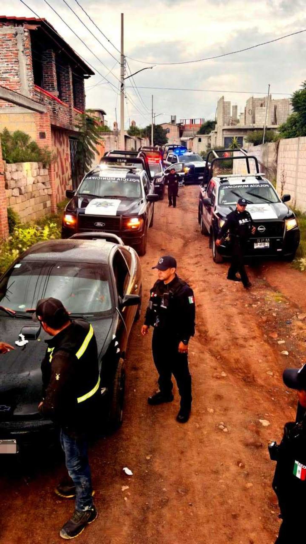 Patrullas de la Polic\u00eda Municipal recorren un camino de terracer\u00eda en una colonia durante un operativo, con oficiales a pie junto a los veh\u00edculos
