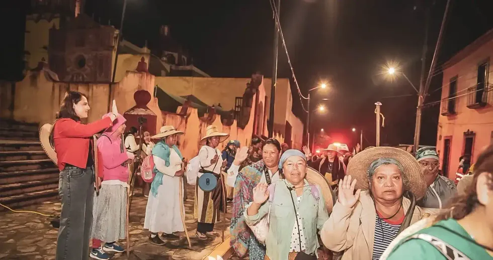 Peregrinas con sombrero de palma caminan de noche por una calle empedrada de Landa de Matamoros durante la peregrinaci\u00f3n al Tepeyac