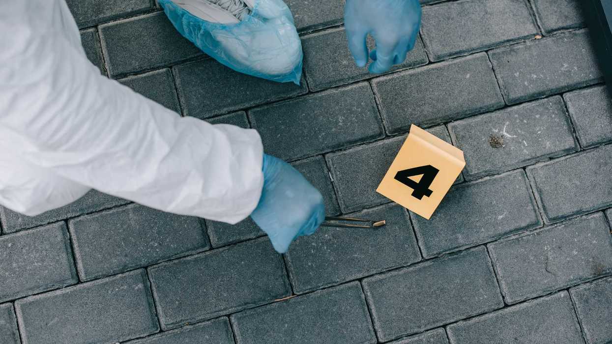 Perito con traje y guantes de protección recoge con pinzas un casquillo junto a un marcador de indicio sobre adoquín, en referencia a los casquillos localizados tras el ataque armado en Juchitán.