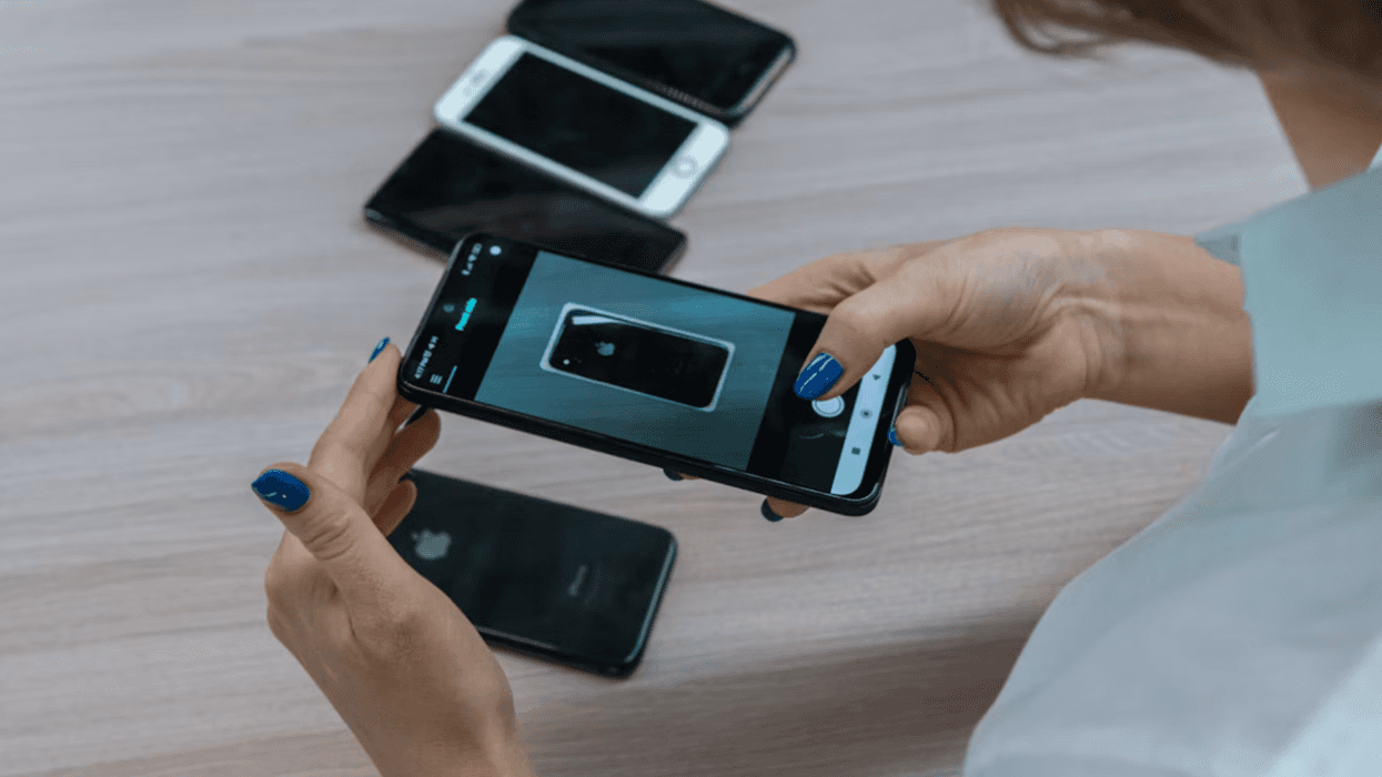 Persona sostiene un smartphone mientras fotografía otro teléfono sobre una mesa con varios celulares, en referencia a la preparación del móvil antes de viajar al extranjero.