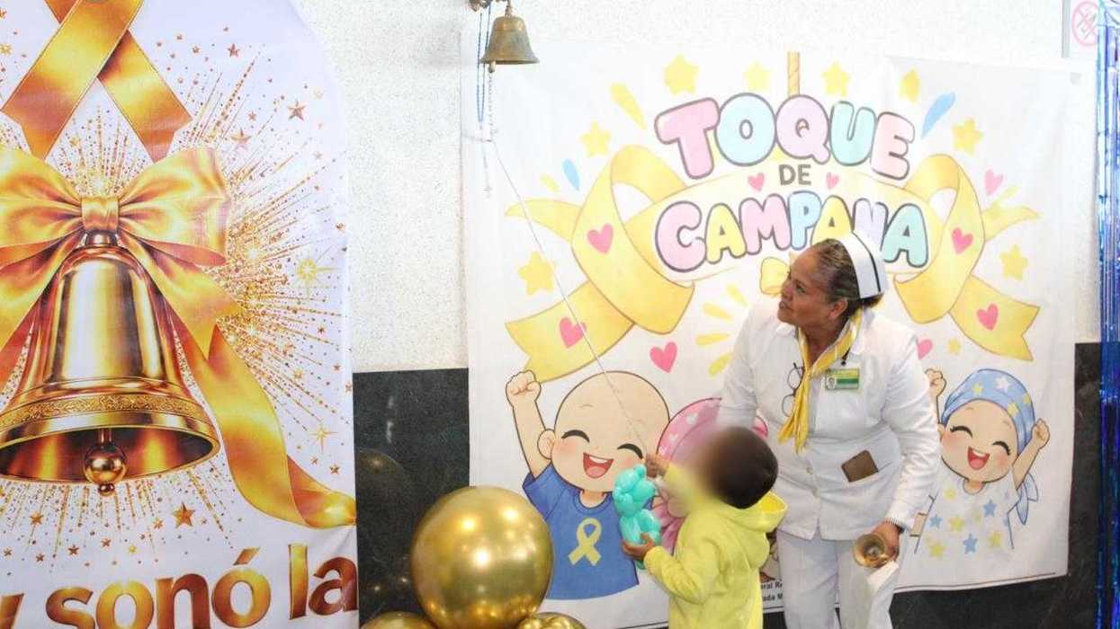 Personal con pañuelos amarillos posa con niños frente a la campana y globos dorados del evento sobre cáncer infantil
