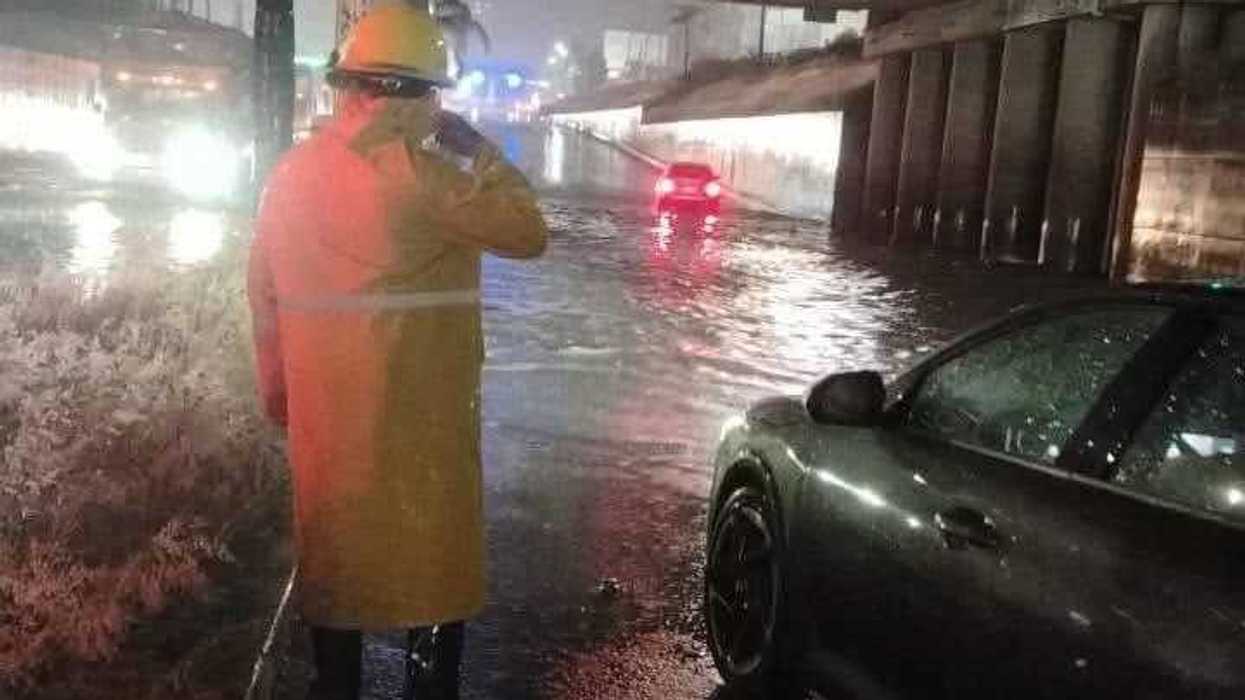 Personal de Protección Civil con impermeable amarillo supervisa una vialidad inundada durante una lluvia intensa