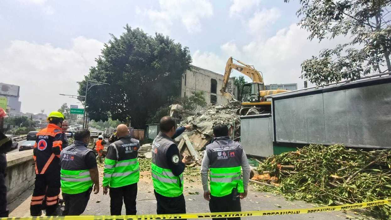 Personal de protección civil observa los escombros de un edificio colapsado durante labores de demolición junto al Viaducto Miguel Alemán, en la colonia Escandón, Ciudad de México, con una excavadora removiendo material entre la vegetación.